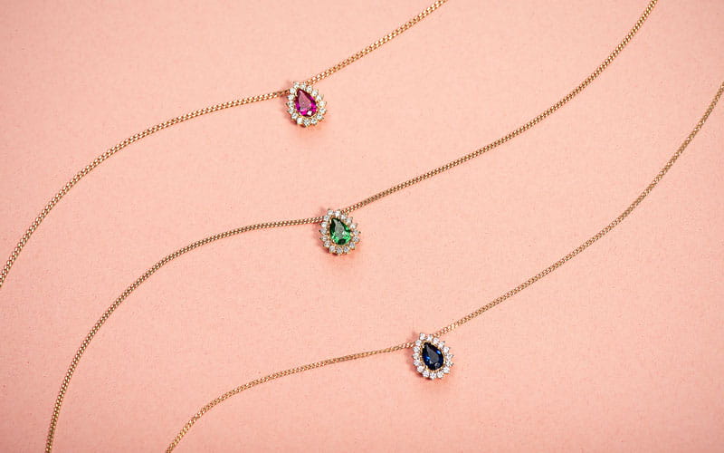 tres colares com pingentes de pedra em formato de gota e fundo rosa