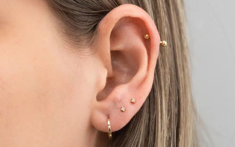 vista de uma orelha feminina com brincos e piercings dourados