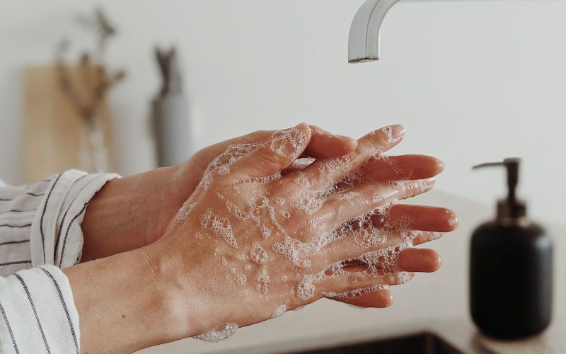 vista lateral de duas mãos femininas sendo lavadas em baixo de uma torneira