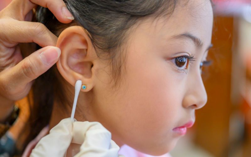Mãos femininas limpando a orelha de uma criança que perfurou as orelhas com um cotonete