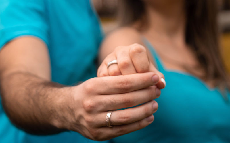 vista de frente de um casal com as mãos entrelaçadas exibindo suas alianças. 