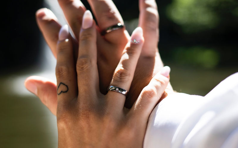 vista de frente de um casal com mãos sobrepostas usando alianças de namoro com pedra