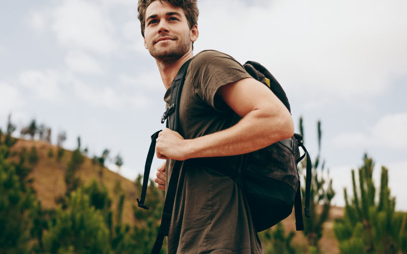 Homem com blusa marrom e uma mochila na costa fazendo uma trilha 